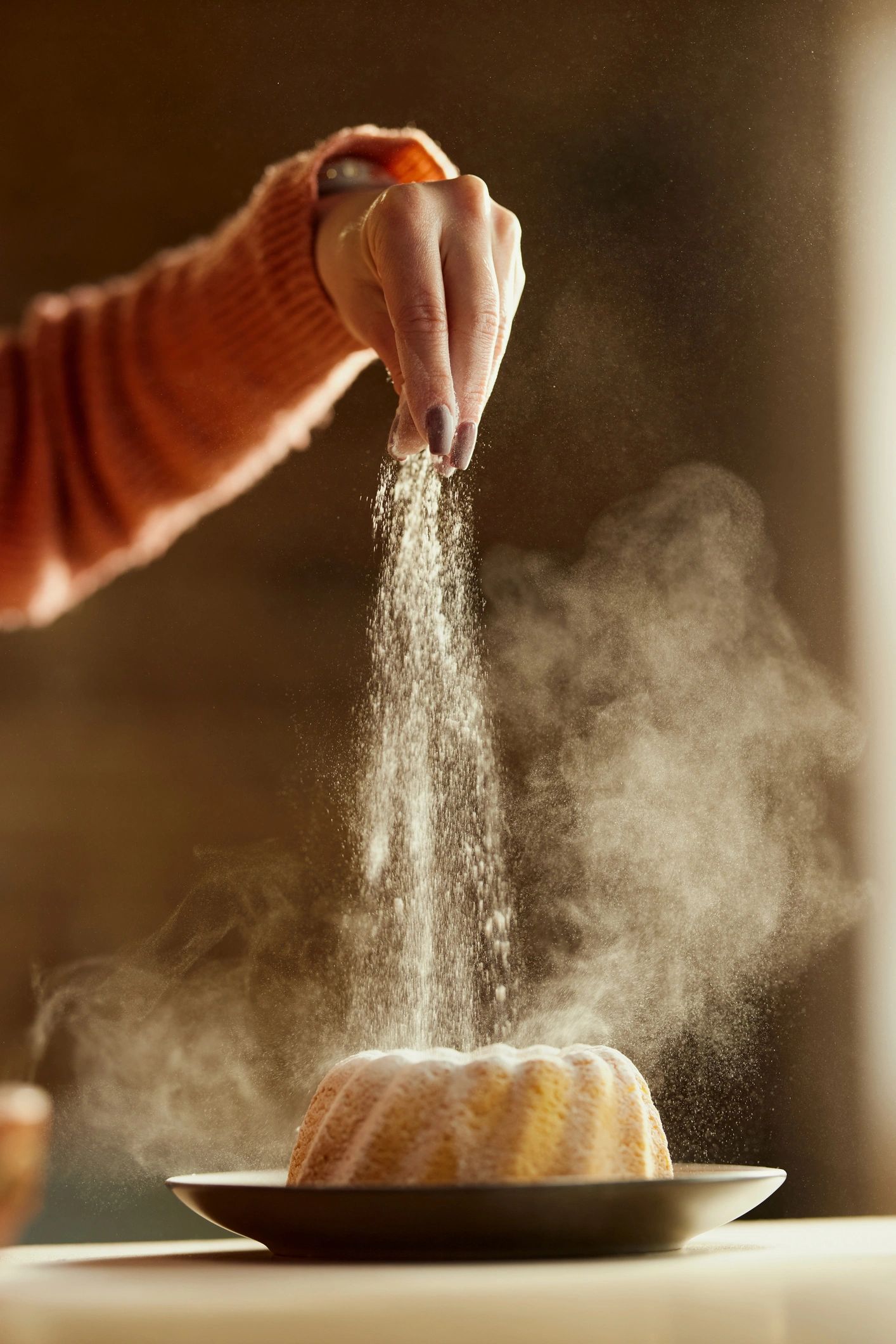 Baker dusting powdered sugar over a freshly baked pastry